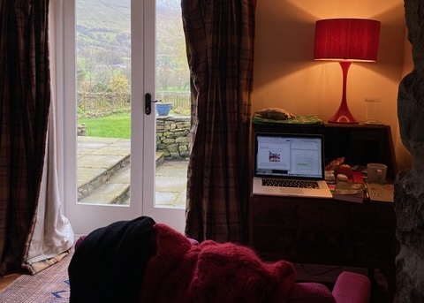 A laptop is open on a desk next to a glass door that leads out onto a view of the Yorkshire Dales